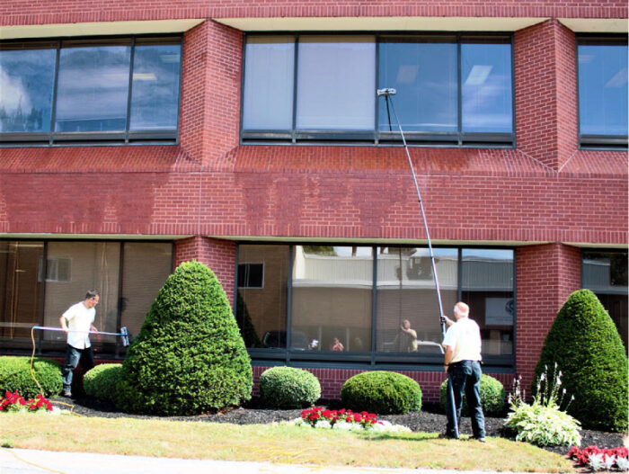 Team of Best View Window Cleaning professionals using water-fed poles to wash the exterior windows of a brick office building in Charlottetown.