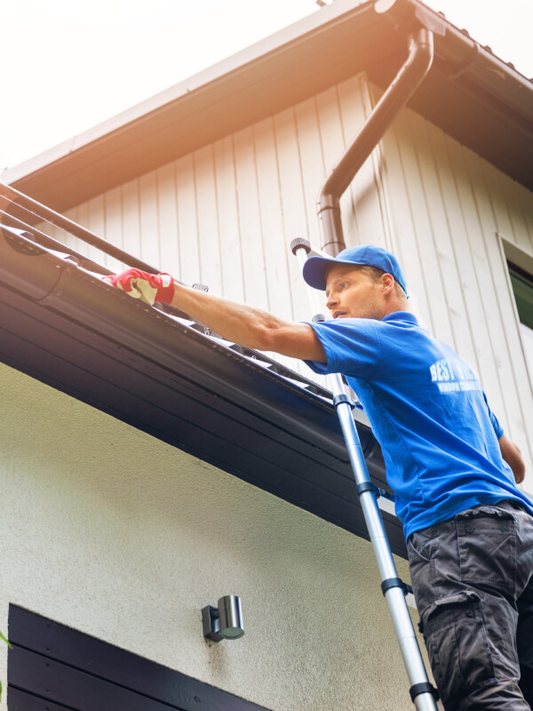 A professional in a blue uniform cleaning eaves-troughs on a ladder in Charlottetown.
